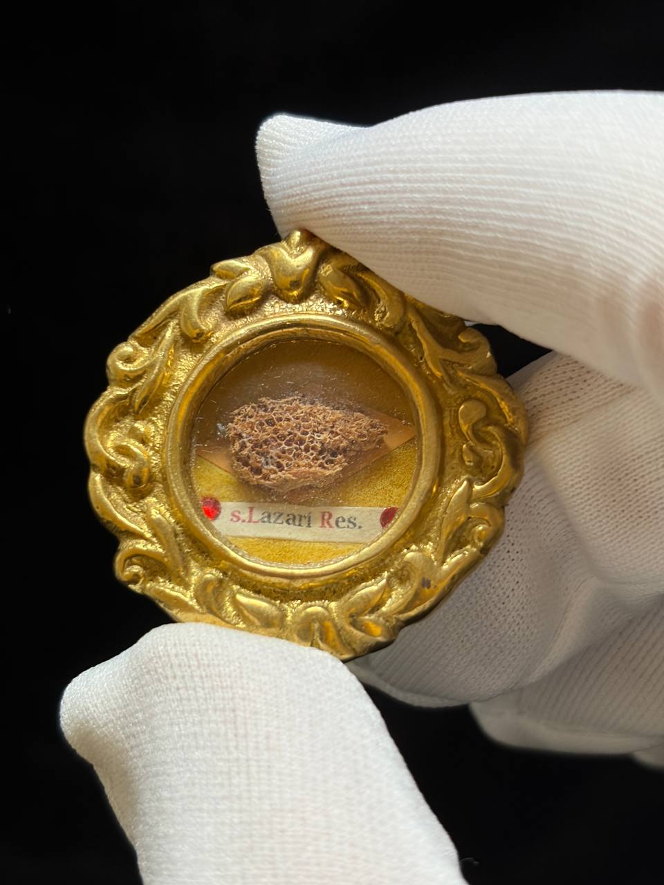 Saint Lazarus of Bethany relic in an ornate gilt theca, label S. Lazari Ep., held in a white glove, close-up