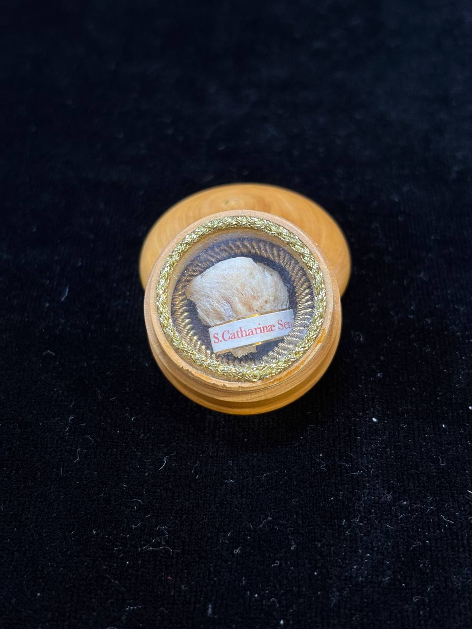 Saint Catherine of Siena relic in a round turned wooden theca with gilt rim, label S. Catharinae Sen., on dark velvet