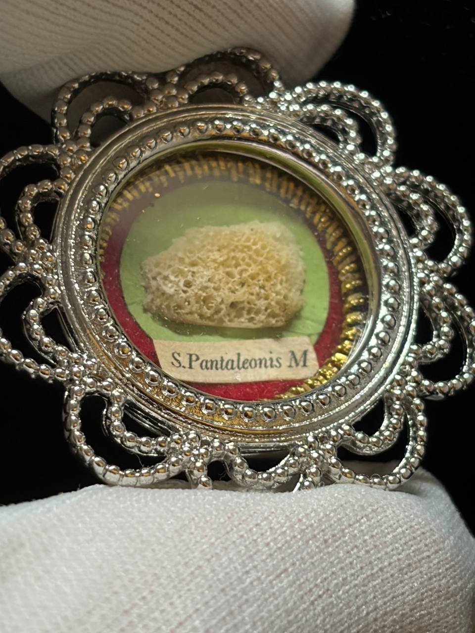 Saint Pantaleon relic in a silver filigree theca, label S. Pantaleonis M., held in a white glove, close-up of the bone relic