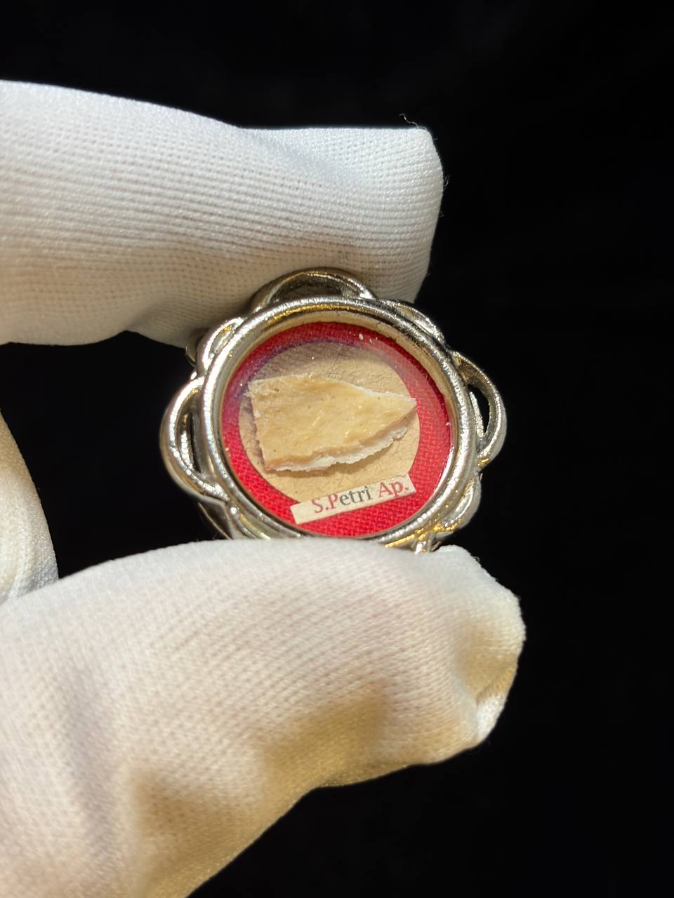 Saint Peter the Apostle relic in a silver quatrefoil theca, label S. Petri Ap., held in a white glove, angled view