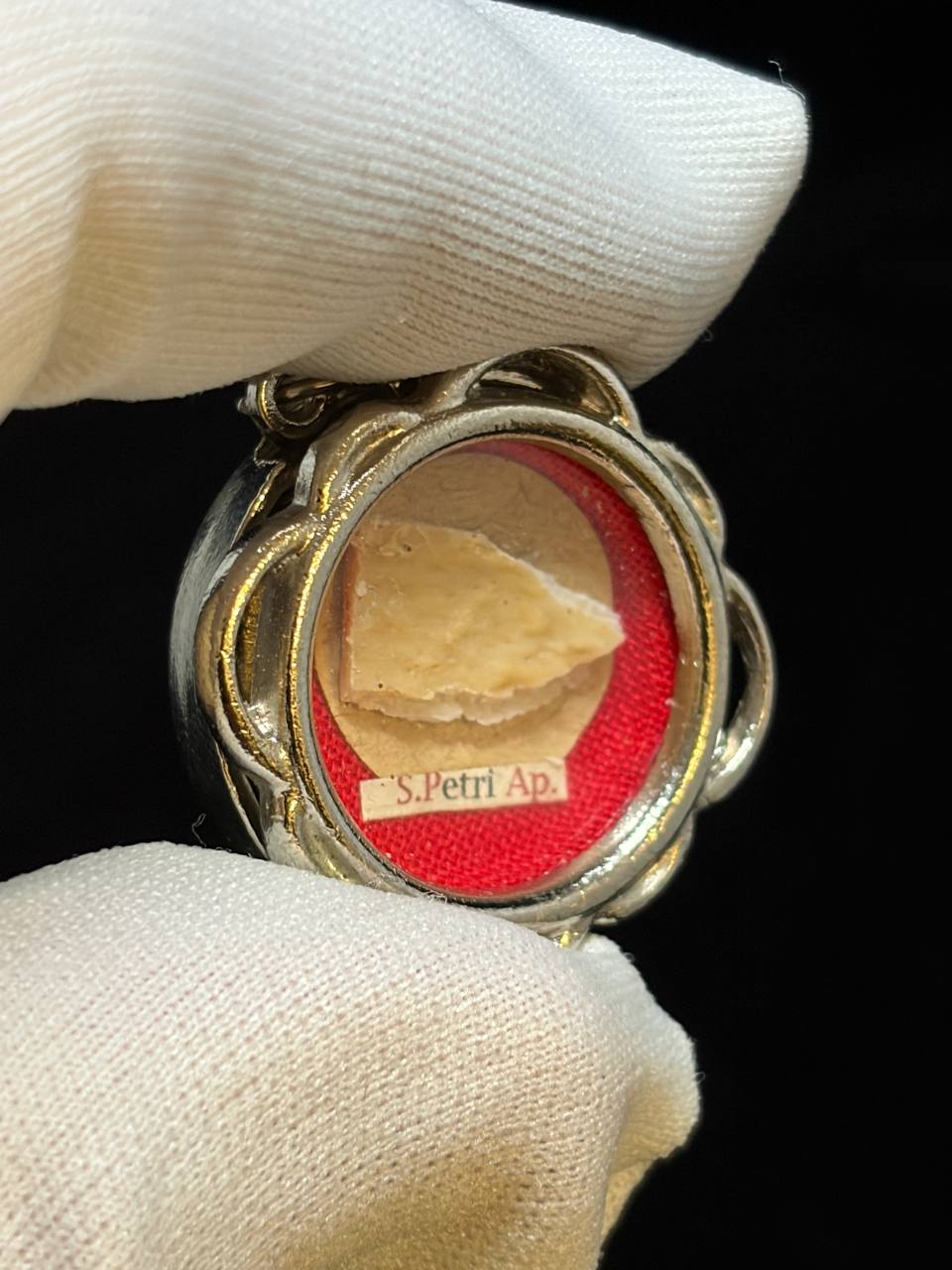 Saint Peter the Apostle relic in a silver quatrefoil theca, label S. Petri Ap., held in a white glove, close-up of the bone relic