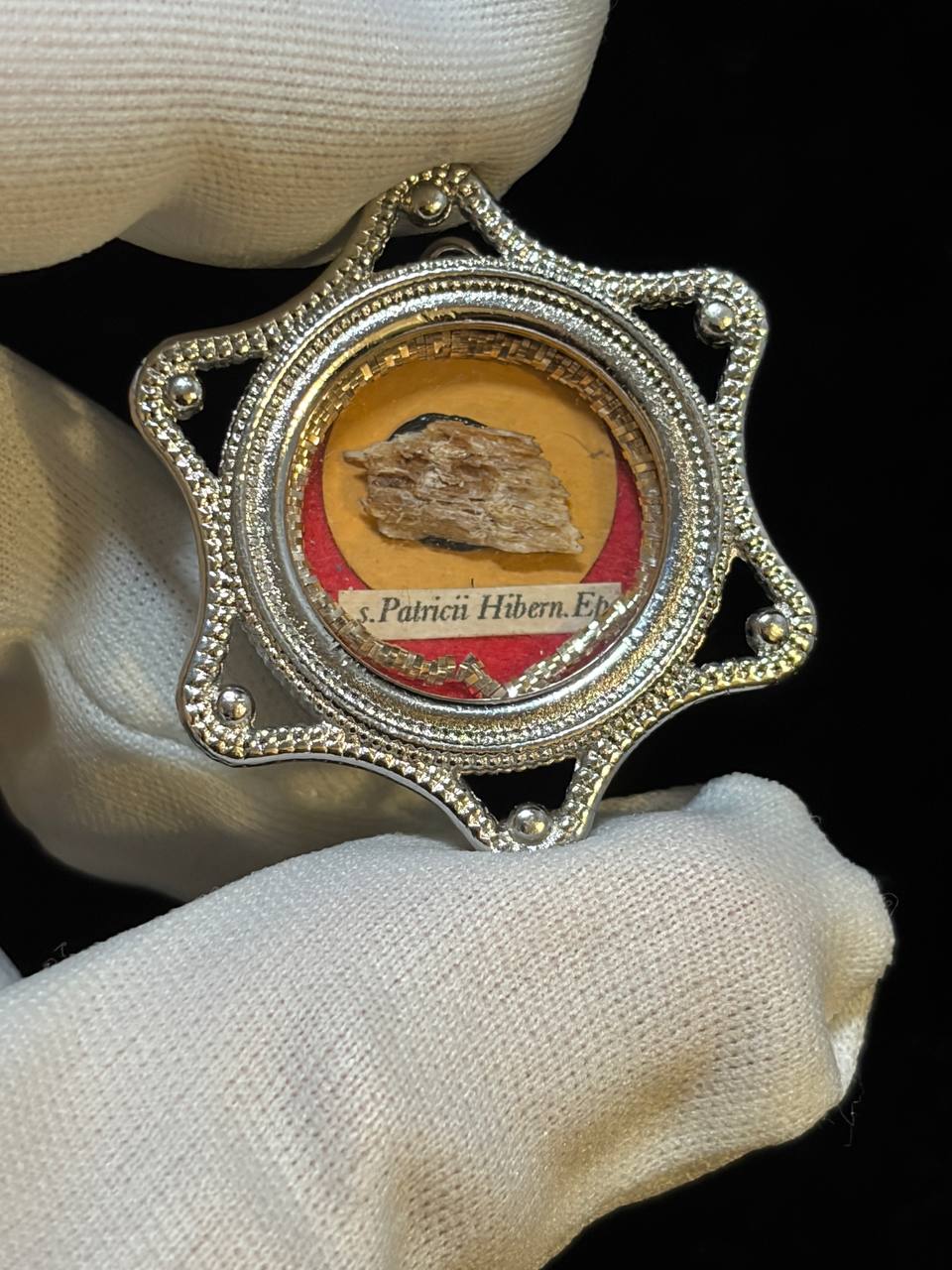 Saint Patrick of Ireland relic in a silver star-shaped theca, label S. Patricii Hiben. Ep., held in a white glove, close-up