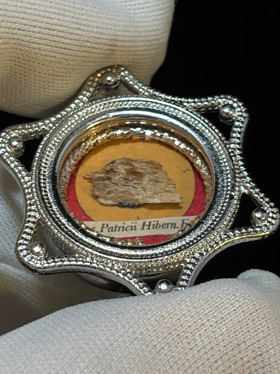 Saint Patrick of Ireland relic in a silver star-shaped theca, label S. Patricii Hiben. Ep., held in a white glove, angled view