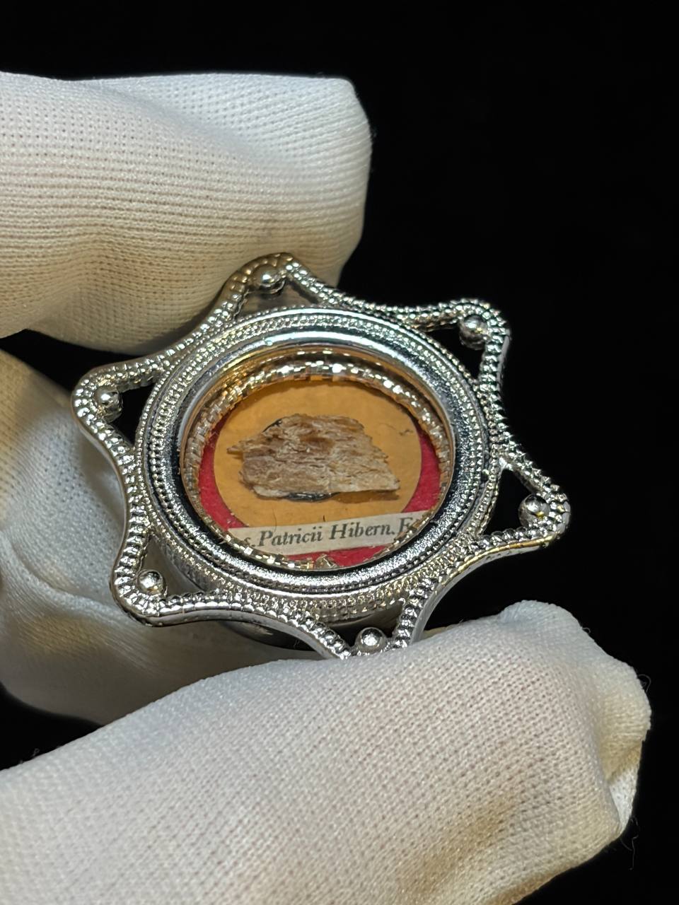 Saint Patrick of Ireland relic in a silver star-shaped theca, label S. Patricii Hiben. Ep., held in a white glove, side view