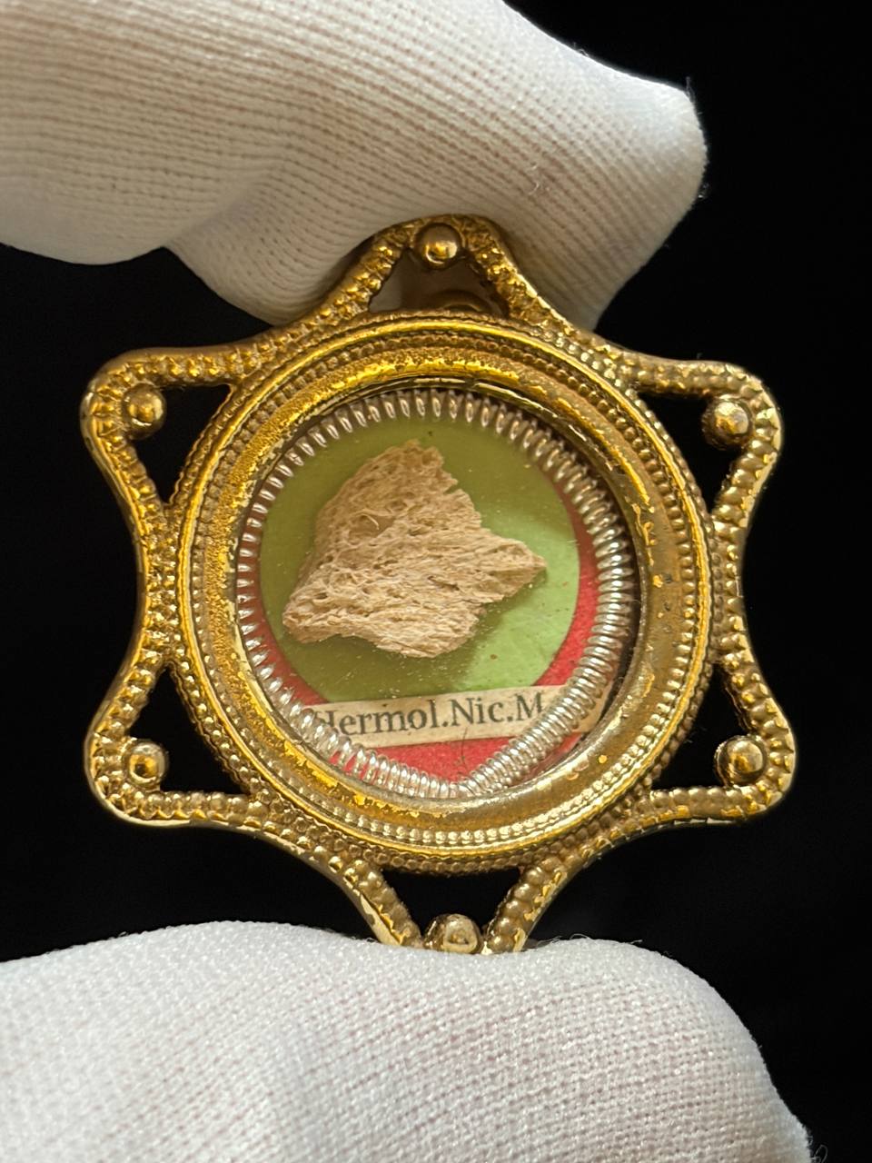 Saint Hermolaus of Nicomedia bone relic on green silk in a gilt star-shaped theca, held in a white glove
