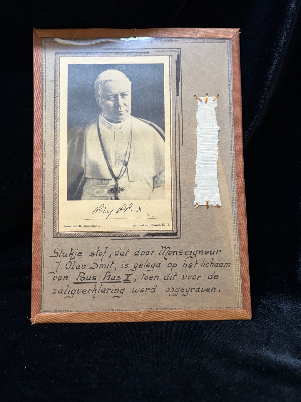 Front of the Saint Pius X contact relic mount with strip of white cloth stitched in gold thread beside the Pope's portrait