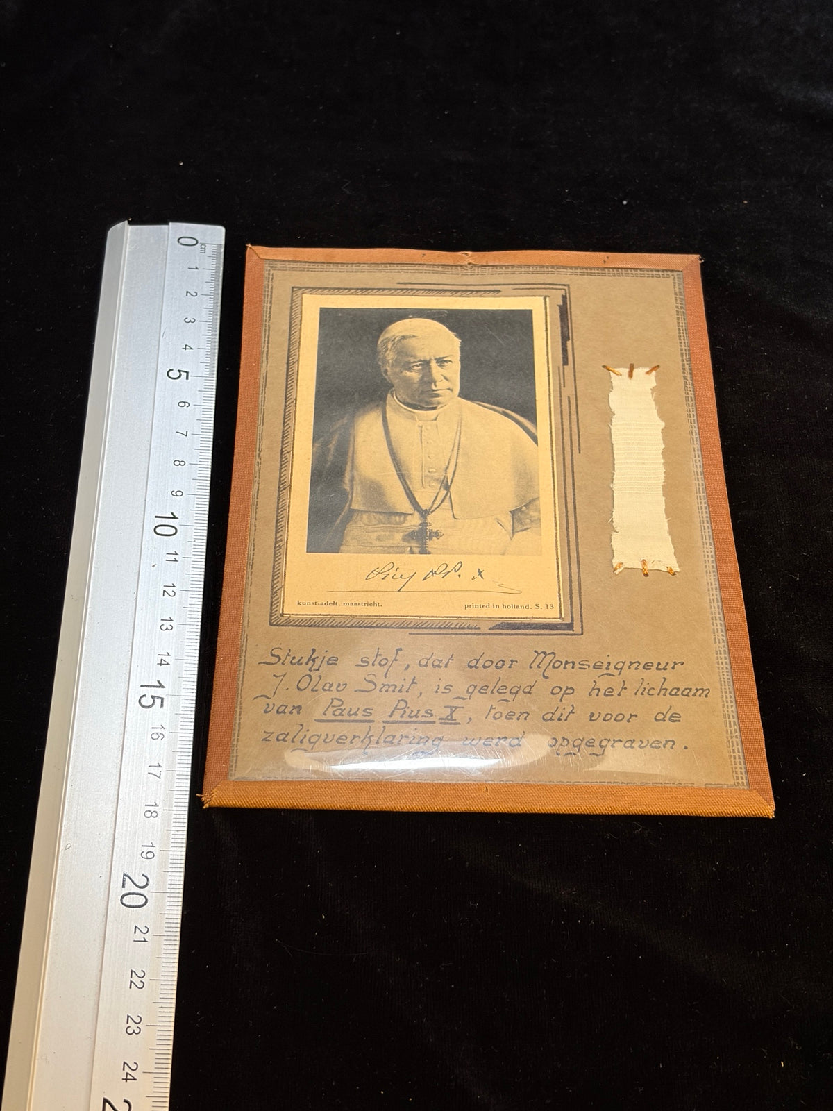 Saint Pius X contact relic next to a ruler showing its size, about 13 x 18.5 cm
